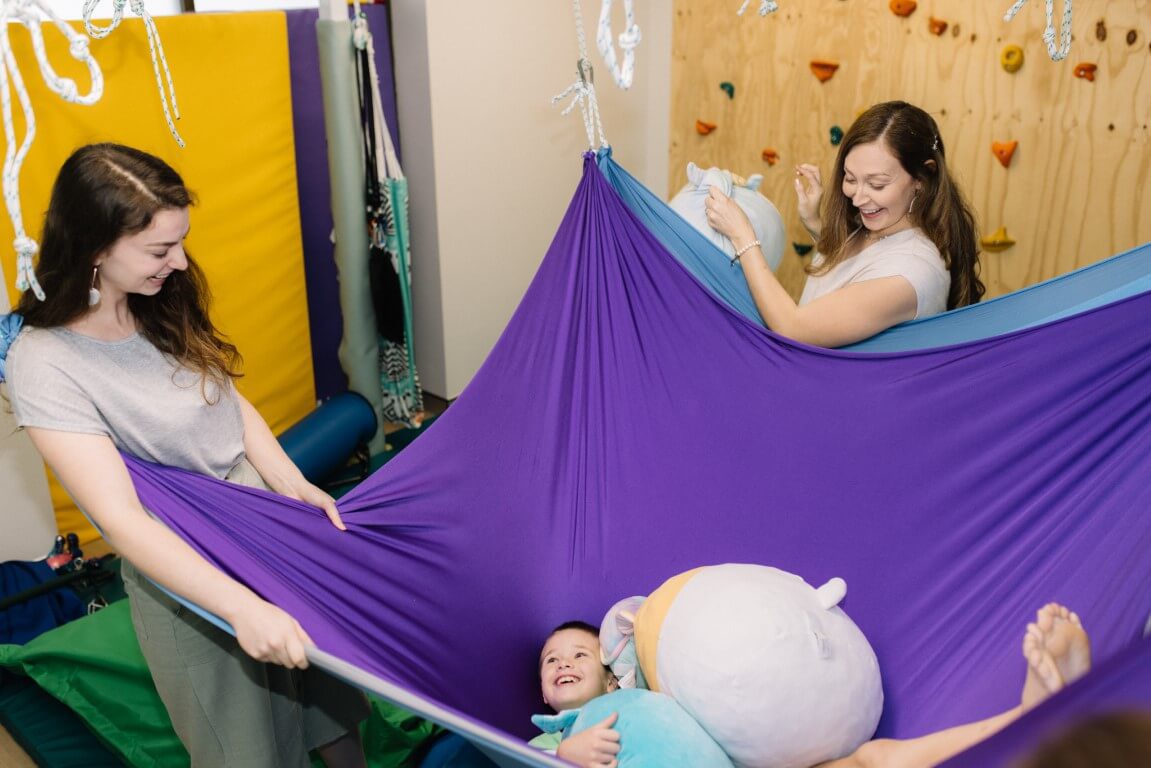 Boy playing in stretchy swing with two therapists